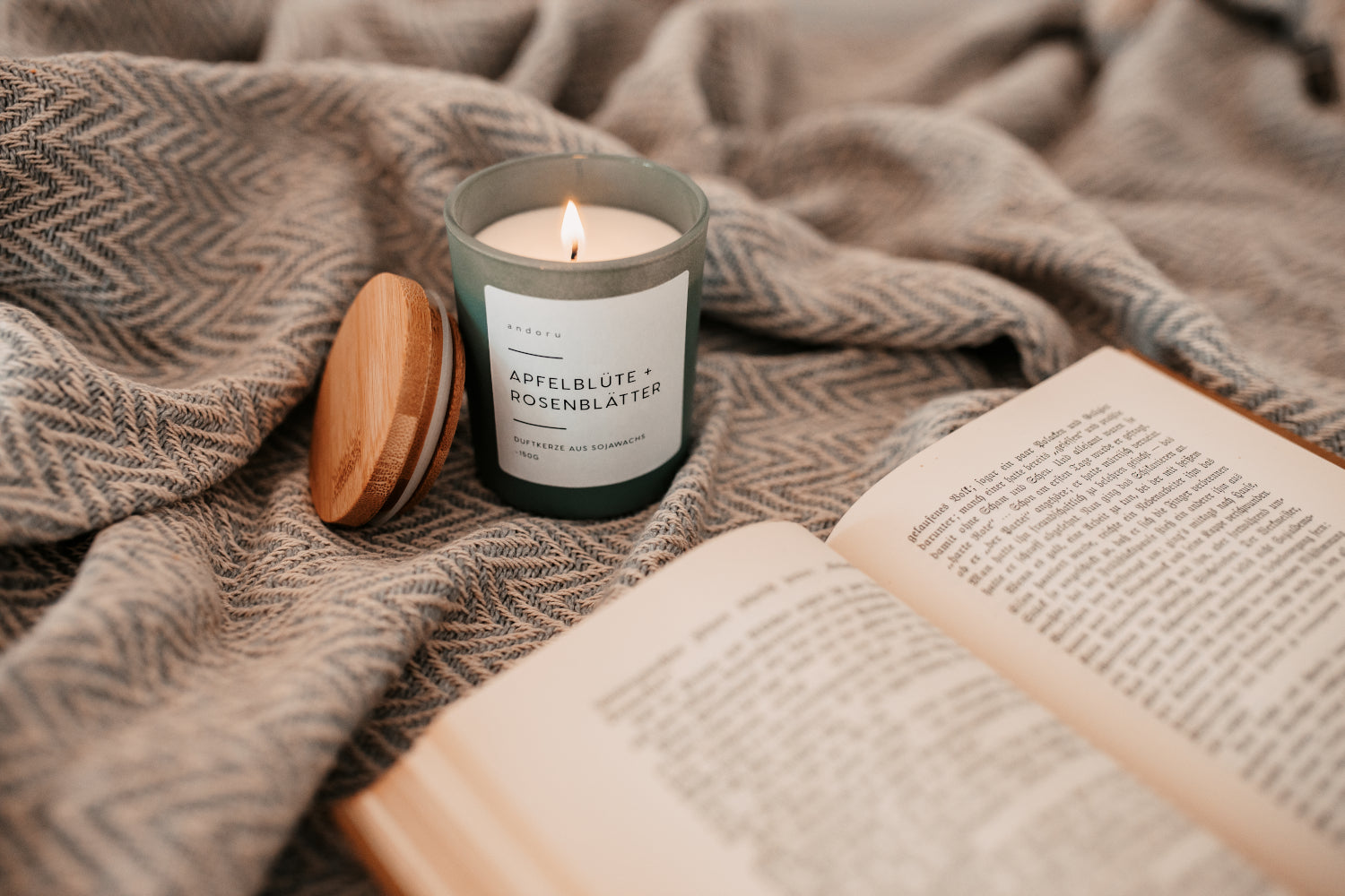 Apfelblüte + Rosenblätter - andoru Duftkerze angezündet neben einem Buch auf einer Decke